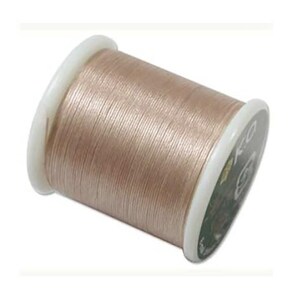 May include: A spool of light beige thread wound tightly around a cylindrical core with white plastic ends. The thread has a subtle sheen and is wrapped in a uniform, horizontal pattern across the entire length of the spool, showing a smooth texture.