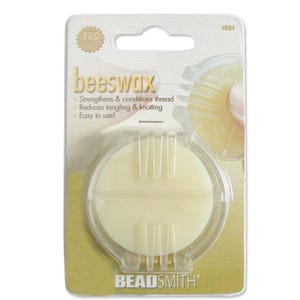 May include: A round, pale yellow disc of beeswax encased in a clear plastic holder on a cardboard backing. The packaging features the text "beeswax", "Strengthens & conditions thread", "Reduces tangling & knotting", "Easy to use!", and "BEADSMITH".