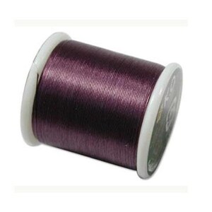 May include: A spool of deep purple sewing thread wound tightly around a white plastic core. The thread has a subtle sheen and is wrapped evenly across the cylindrical spool, which features white circular ends with visible branding text.