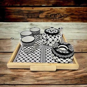 Könnte beinhalten: Ein Tablett aus Holz mit einem schwarz-weißen Muster enthält eine Teekanne, vier Tassen und einen Aschenbecher. Die Tassen und die Teekanne haben ein schwarz-weißes geometrisches Muster.