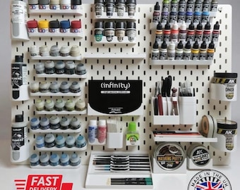 Op de afbeelding: Een witte pegboard met diverse modelbouwverfbenodigdheden. De collectie omvat verfpotjes, penselen, afplakkit en andere gereedschappen. De tekst "(infinity)" is zichtbaar. De afbeelding bevat ook de tekst "FAST DELIVERY".