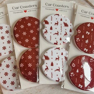 May include: Set of car coasters with festive holiday designs. Each coaster features a unique pattern, including snowflakes, reindeer, and gingerbread men, in red and white. The packaging reads "Car Coasters Handmade with love."