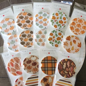 May include: A set of 12 fall-themed car coasters. The coasters feature various designs including pumpkins, leaves, plaid, and stripes. The coasters are handmade with love.