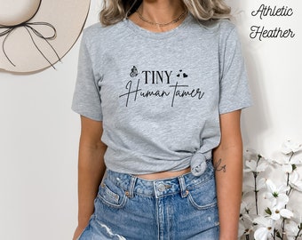 May include: A gray t-shirt with the text "Tiny Human Tamer" and a butterfly graphic. The shirt is made of athletic heather fabric.