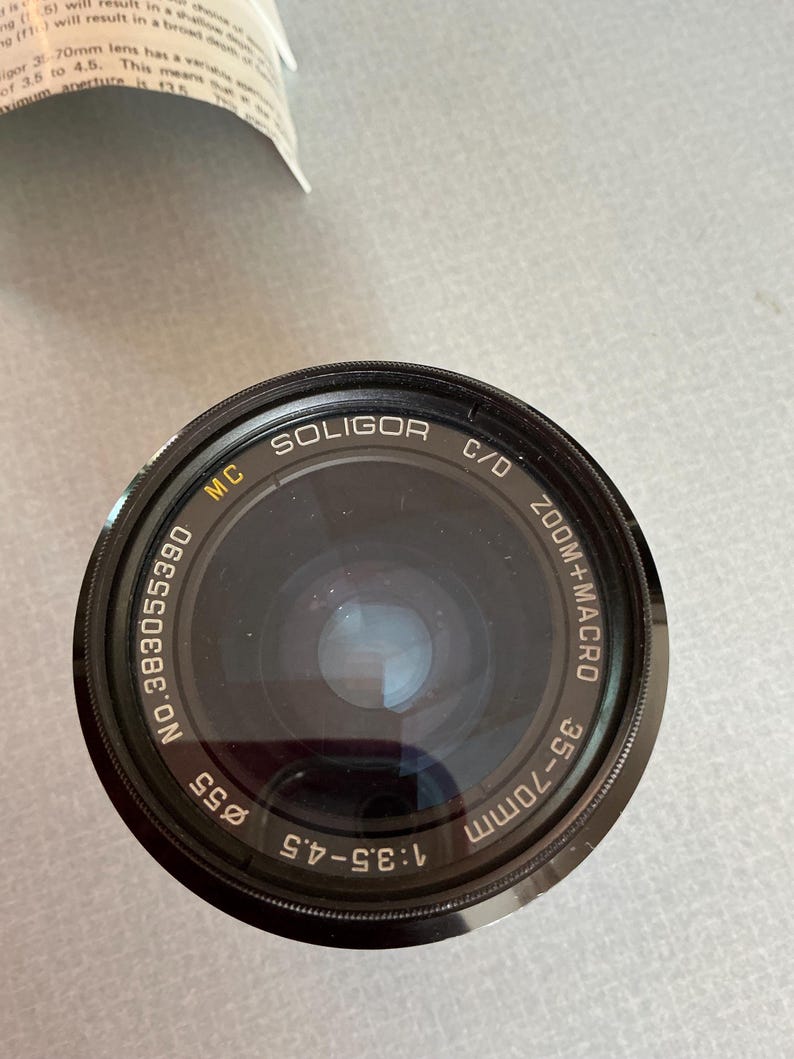 K&ouml;nnte beinhalten: Ein schwarzes Soligor 35-70mm Zoomobjektiv mit Makrofunktion. Das Objektiv hat einen Durchmesser von 55 mm und eine Blende von f/3,5-4,5. Der Text "MC SOLIGOR C/D" ist auf dem Objektiv aufgedruckt.