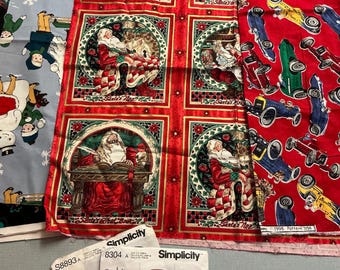 May include: Assorted fabric pieces featuring holiday and children's themes. One fabric has a repeating pattern of Santa Claus in red squares. Another has race cars on a red background. Sewing patterns for baby clothes are also visible.
