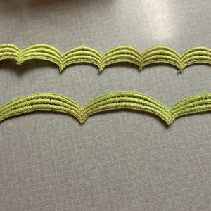 May include: Two strips of light green scalloped trim. The trim has a textured, embroidered appearance with a repeating wave pattern. The trim is likely used for sewing or crafting projects.