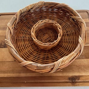 May include: A brown wicker basket with a smaller wicker basket inside. The baskets are woven together and have a natural finish.