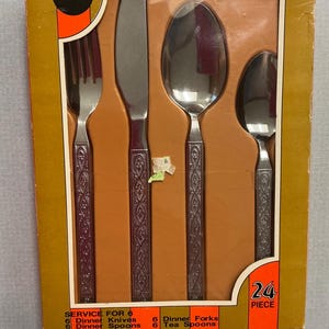 May include: A boxed set of Bonanza silverware, featuring a fork, knife, spoon, and teaspoon. The handles have an ornate design. The box is orange and brown, with text indicating a 24-piece set, service for 6.