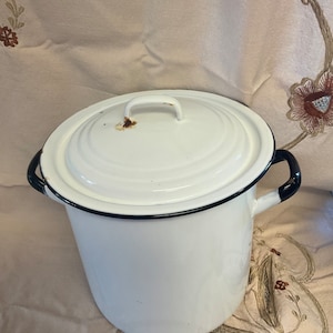 May include: White enamelware pot with a black rim and black handles. The pot has a lid with a black rim and a small handle.