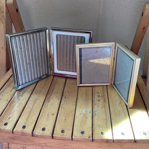 May include: Three silver and gold picture frames with a wood grain background. The frames are open and ready to display photos.