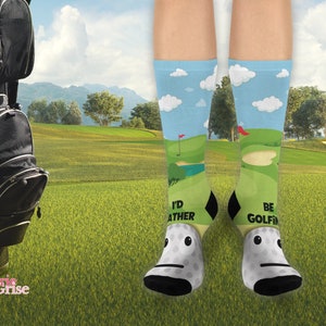 May include: A pair of white socks with a golf course design. One sock says "I'd Rather Be Golfing" and the other says "Be Golfing".