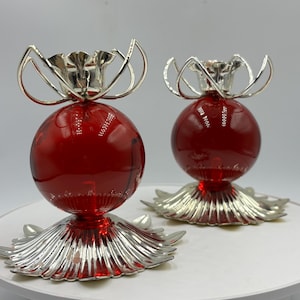 May include: A pair of red glass candle holders with silver metal bases and decorative floral tops.