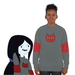Puede incluir: Una sudadera gris con mangas rojas y un gráfico de cara de gato rojo en la parte delantera. El gato tiene ojos amarillos y una nariz rosa.