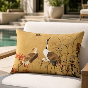 May include: Rectangular decorative pillow with a mustard yellow background featuring a Japanese-style illustration of two cranes and foliage. The pillow is placed on a white chair, suggesting outdoor use.
