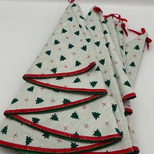 May include: Set of six white fabric Christmas tree skirts with a green and red trim. The skirts are decorated with a repeating pattern of green Christmas trees and red dots.