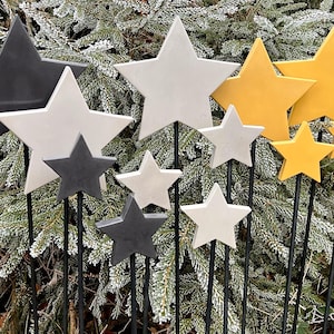 Könnte beinhalten: Ein Set mit 10 dekorativen sternförmigen Gartenpfählen in Schwarz, Weiß und Gelb. Die Sterne sind aus keramikähnlichem Material gefertigt und an schwarzen Metallpfählen befestigt.