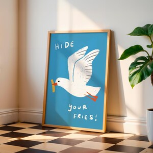 A cheeky seagull eyes a pile of fries in this vibrant, maximalist illustration, bursting with bold colors and playful text warning to protect your snacks. Perfect for adding a humorous coastal vibe to kitchens, beach house nooks, or sunny living spaces. Quirky vacation art, funny home accent, dopamine decor gift, coastal wall hanging, playful beachy print. Ideal for fry-loving friends or anyone craving a lighthearted, maximalist touch to their decor. Frame it for a pop of joy in any room.