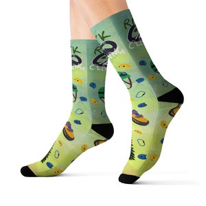 May include: A pair of socks with a light green gradient background, featuring climbing-themed graphics. The socks display climbing shoes, holds, and the text "ROCK CLIMBING CLUB". The socks have black heels and toes.