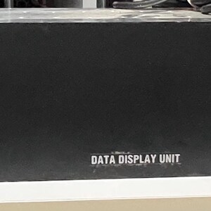 May include: A black data display unit with silver handles and a power switch. The unit has the words "DATA DISPLAY UNIT" printed on the front. The power switch is on a small silver plate.