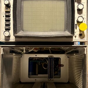 May include: Vintage Hewlett-Packard 184A oscilloscope. The device has a rectangular screen with a grid pattern, surrounded by control knobs and switches. The lower section reveals internal components, including wiring and connectors. The device is labeled with the Hewlett-Packard logo.