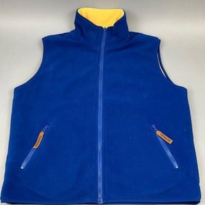 Puede incluir: Un chaleco de forro polar azul con forro de polar amarillo. El chaleco tiene cierre de cremallera y dos bolsillos con cremallera.