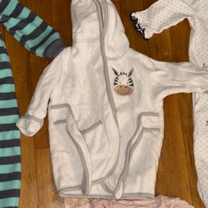 May include: A white ceramic mug with a black handle and the text "But First, Coffee" in a black, bold font. The mug is sitting on a white surface. The mug is approximately 4 inches tall.