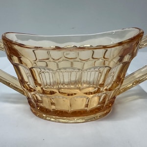 May include: A vintage, amber-colored glass sugar bowl with two handles. The bowl has a textured, geometric design.