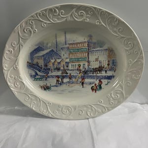 Puede incluir: Plato ovalado de cerámica blanca con un diseño floral en relieve alrededor del borde. El centro del plato presenta una escena de invierno con una ciudad, personas patinando sobre hielo y el texto "Procter & Gamble" y "Soap & Candles".