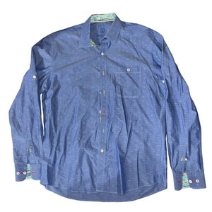 May include: A blue long-sleeved button-down shirt with a white polka dot pattern. The shirt has a colorful patterned inner collar and cuffs.