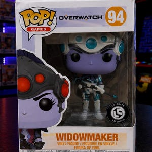 May include: A Funko Pop! Games Overwatch Widowmaker vinyl figure in a display box. The figure is purple, white, and blue, holding a rifle. The box features the Overwatch logo, the number 94, and the Loot Crate Exclusive logo.