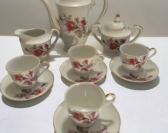 May include: A vintage porcelain tea set with a floral design. The set includes a teapot, creamer, sugar bowl, and four teacups and saucers. The cups and saucers have a delicate floral pattern with pink roses and green leaves on a white background.
