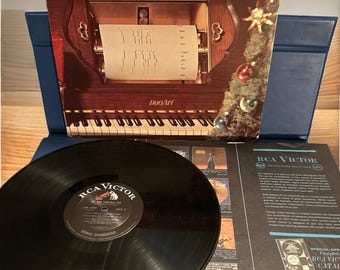 May include: A vintage vinyl record album cover featuring a piano roll player with a Christmas tree in the background. The album title is "The Piano Rolls and Voices All Time Christmas Hits" and the record label is RCA Victor.