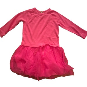 Puede incluir: Un vestido rosa de manga larga con falda de tul. El vestido tiene un escote redondo y un cordón en la cintura.