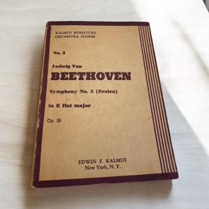 May include: A brown paper book cover with a maroon border. The title is "Ludwig Van Beethoven Symphony No. 3 (Eroica) in E flat major Op. 55" and the publisher is "Edwin F. Kalmus New York, N. Y."