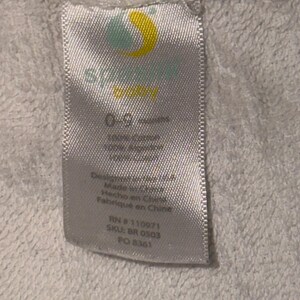 May include: A white fabric tag with the brand logo and text. The tag includes the text "0-9 months", "100% cotton", and "100% acrylic". Additional text includes "Designed in USA", "Made in China", "Hecho en China", and "Fabriqu&eacute; en Chine".