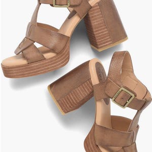 Op de afbeelding: Een paar bruine leren sandalen met een dikke blokhak met geribbelde textuur, een plateauzool en een verstelbare enkelband met een messingkleurige metalen gesp. De sandalen hebben brede, gekruiste bandjes over het teengedeelte.