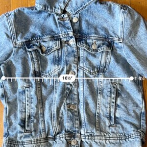 May include: Light blue denim jacket with button closures, two chest pockets, and two side pockets. The jacket measures 41.9 cm across the chest. The jacket is 41.9 cm in length.