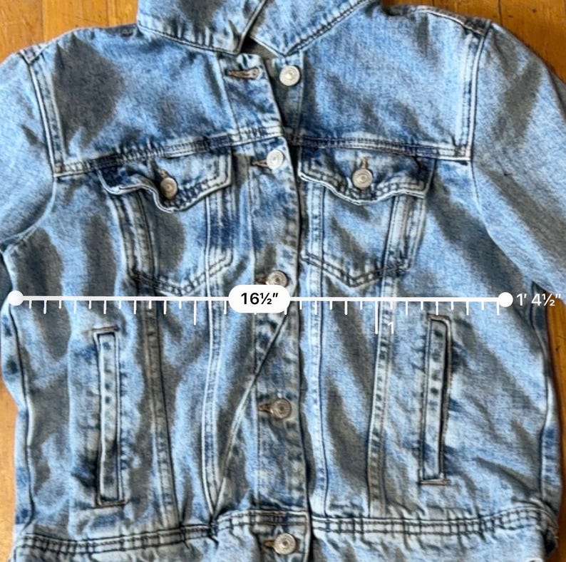 May include: Light blue denim jacket with button closures, two chest pockets, and two side pockets. The jacket measures 41.9 cm across the chest. The jacket is 41.9 cm in length.