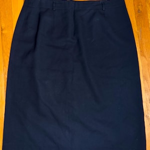 May include: A navy blue skirt with a straight silhouette. The skirt has a waistband with belt loops and a button closure. The fabric appears to be a medium-weight material, suitable for various occasions.
