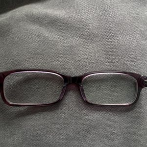 May include: Rectangular eyeglasses with a dark purple frame. The lenses are clear, and the glasses are set against a gray fabric background. The frames have a subtle, glossy finish.