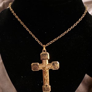Könnte beinhalten: Eine goldene Kettenkette mit einem detaillierten, verzierten goldenen Kreuzanhänger. Das Kreuz zeigt auf der Vorderseite eine Darstellung von Jesus Christus und auf der Rückseite komplizierte Designs.