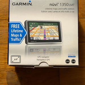 Puede incluir: Una caja de navegador GPS Garmin nüvi 1350LMT. La caja muestra el logotipo de Garmin, detalles del producto y una pantalla con un mapa. Incluye el texto "¡Mapas y tráfico de por vida GRATIS!" y una pantalla de 4,3 pulgadas.