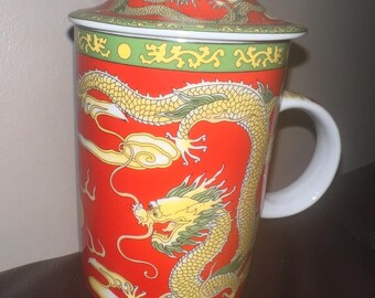 Puede incluir: Una taza de té de cerámica roja con tapa, con un diseño de dragón amarillo. La taza tiene un asa blanca y un botón blanco en la tapa. El dragón está detallado con detalles verdes, y la tapa tiene un borde verde y rojo.
