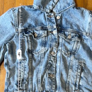 May include: Light blue denim jacket with a classic collar, button-down front, and multiple pockets. The jacket is approximately 45.7 cm long. The denim has a faded, worn look.