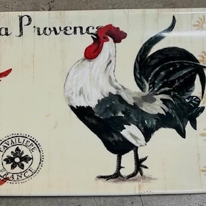 Puede incluir: Bandeja rectangular con ilustración de gallo. La bandeja presenta un fondo crema con un gallo en el centro, rodeado de motivos florales y decorativos en rojo y beige. Las palabras "la Provence" están impresas en la bandeja.
