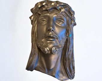 Könnte beinhalten: Eine silberfarbene Skulptur eines Männergesichts mit einer Dornenkrone. Die Skulptur ist detailliert und realistisch, mit einem traurigen Ausdruck im Gesicht des Mannes.