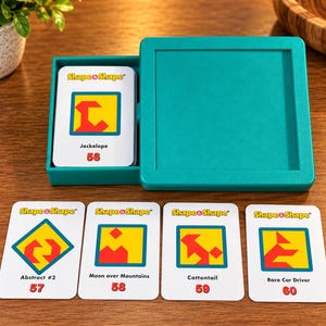 May include: A teal plastic storage box containing a deck of Shape & Shape cards, with four additional cards labeled Abstract #2, Moon over Mountains, Cottontail, and Race Car Driver displayed in front, each featuring colorful geometric shapes.