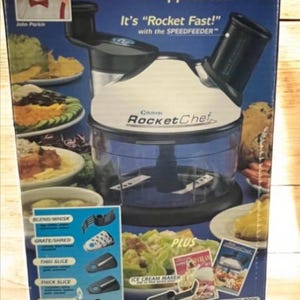 May include: A Rocket Chef kitchen appliance box. The box is blue with the words "Rocket Chef" in red and white. It includes a food processor, a bonus fat-free gourmet pan, and an ice cream maker. The box says it replaces a kitchen full of appliances.