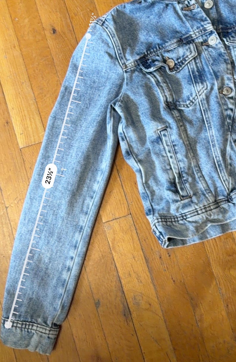 May include: Light blue denim jacket with a classic design. The sleeve length is 59.69 cm. Features include a button-up front, chest pockets, and a collar. The jacket is made of a light-wash denim material.